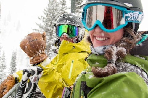 Two people smiling covered in snow on the chairlift