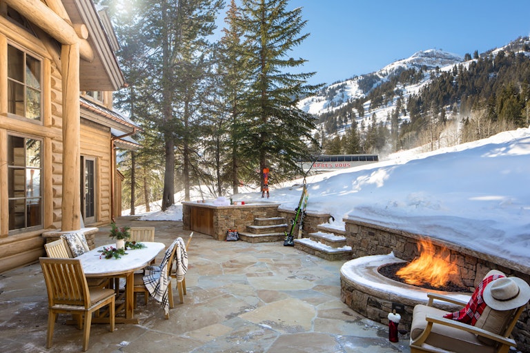 Slope side stone patio with a lit fireplace