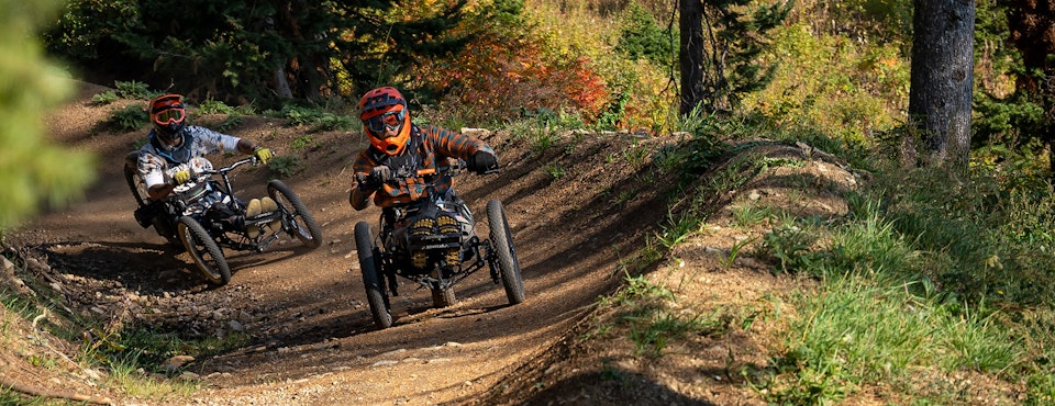 Two adaptive bikers going down a challenging Bike Park trail