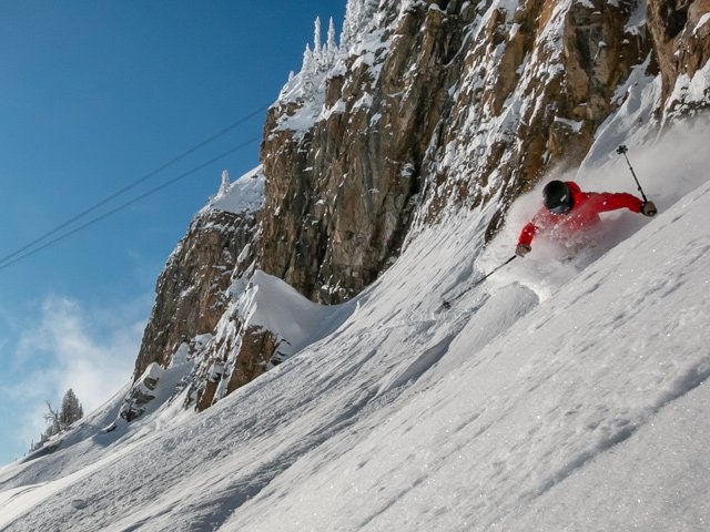 Man skiing down powder field under a clif