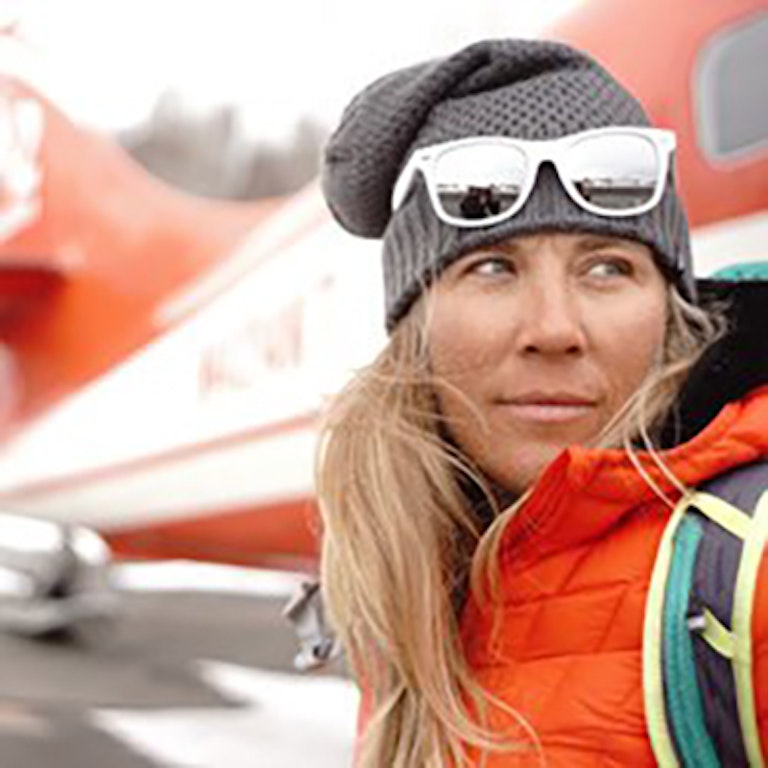 Jess McMillan looking off in the distance standing in front of a helicopter