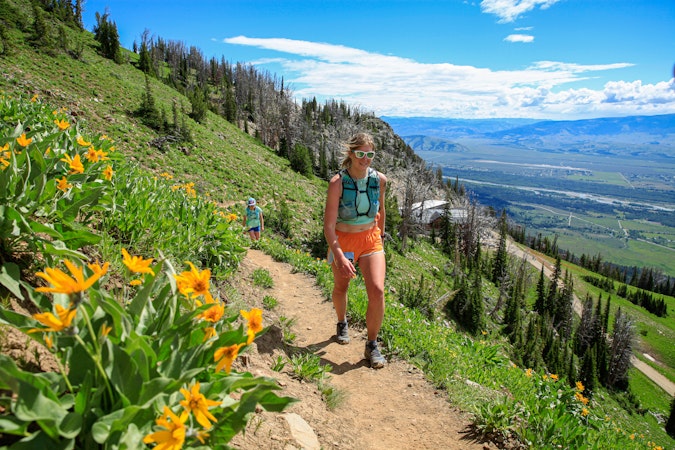 woman hiking on trail next to flowers