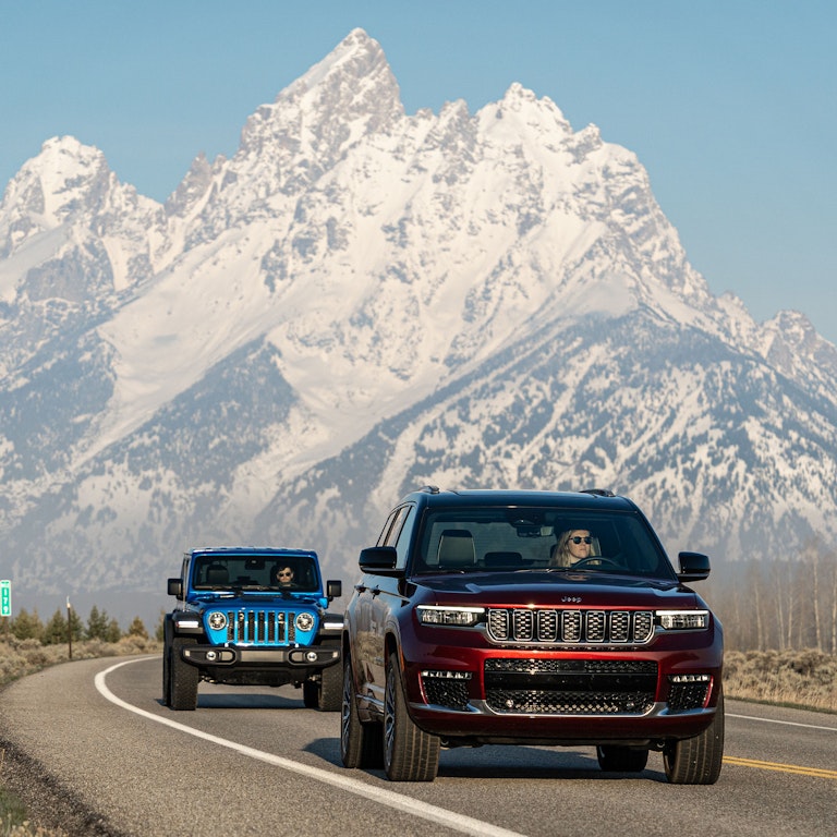 Two jeeps driving down road with the Grand Teton in the background