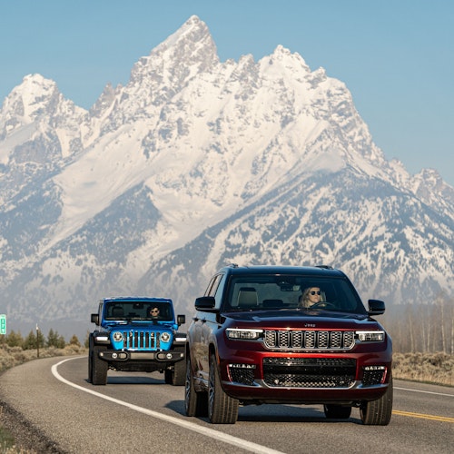 Two jeeps driving down road with the Grand Teton in the background