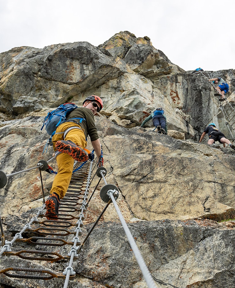 man walking up ladder on the Via Ferrata with rest of group ahead of him