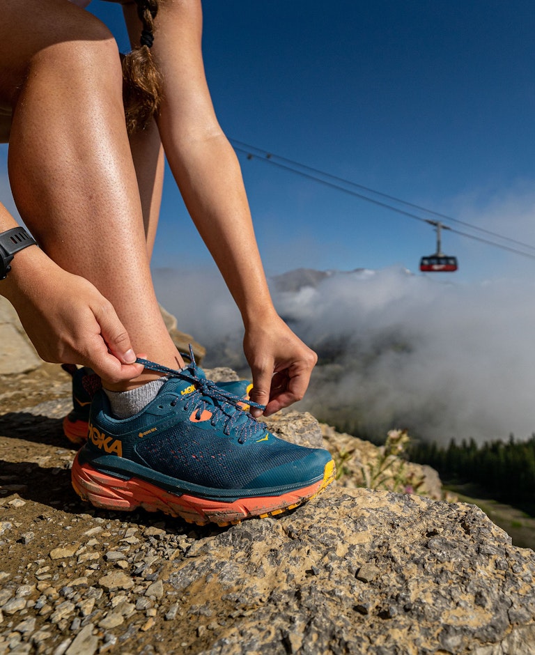 Hiker tying her GORE-TEX shoes with the Aerial Tram in the background