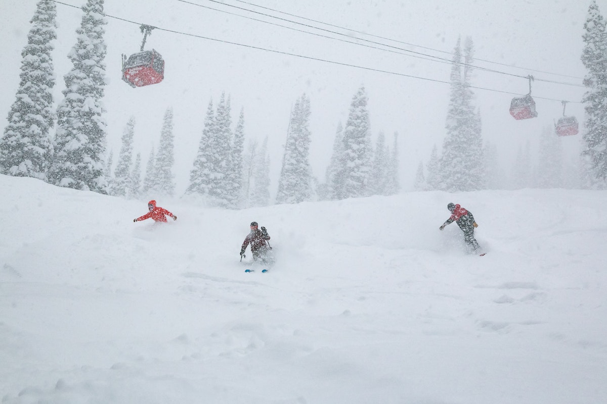 Two snowboarders and a skier in powder under the gondola