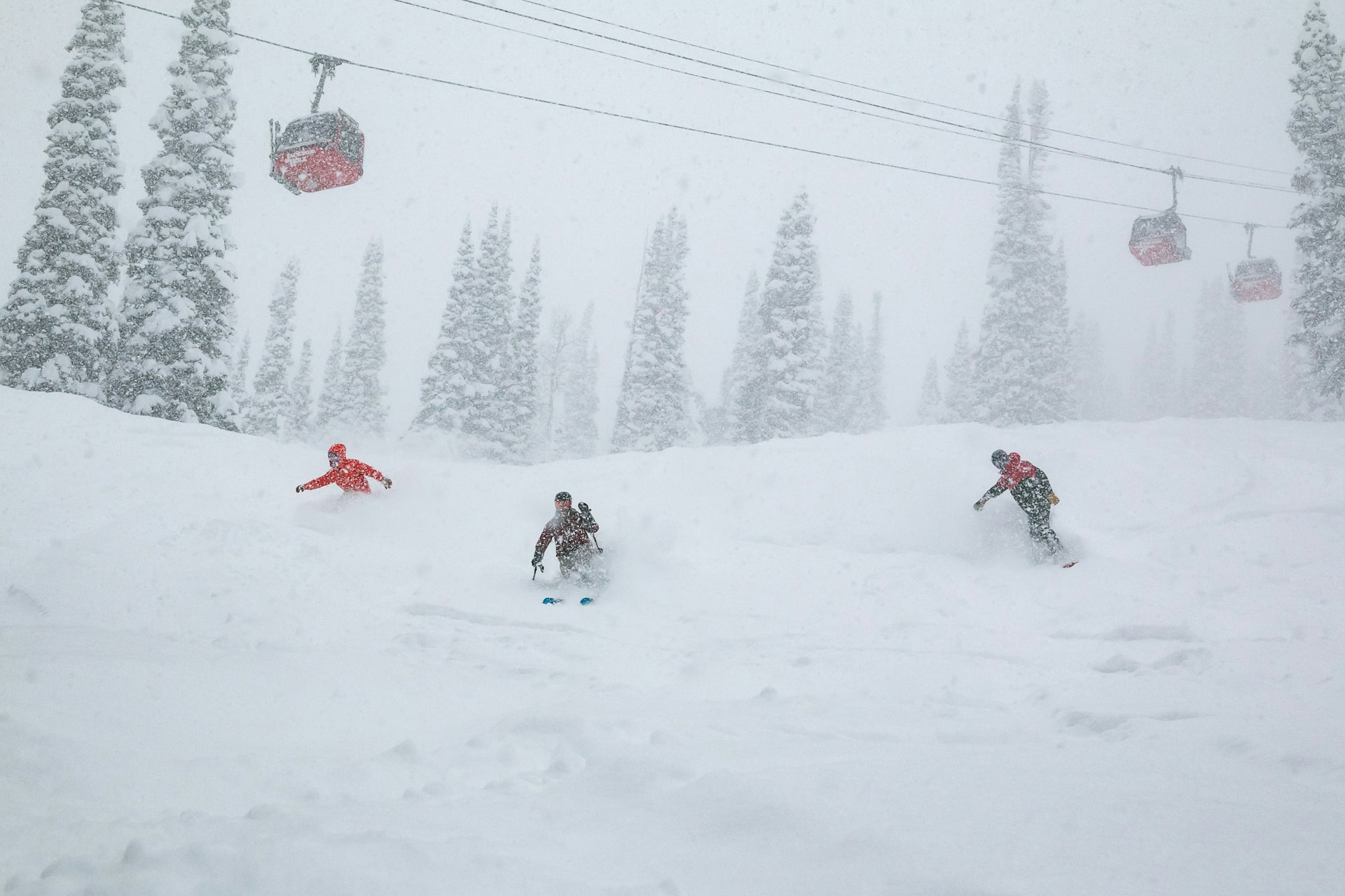 Two snowboarders and a skier in powder under the gondola