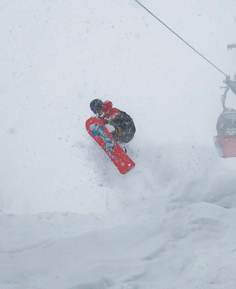 Snowboarder jumping off a rock covered in powder