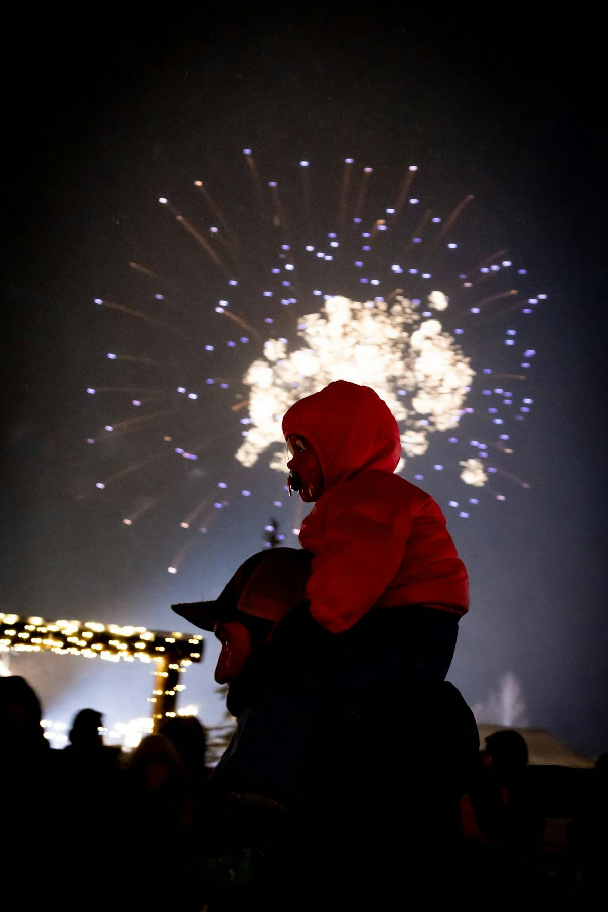 Kid on fathers shoulders with fireworks in background
