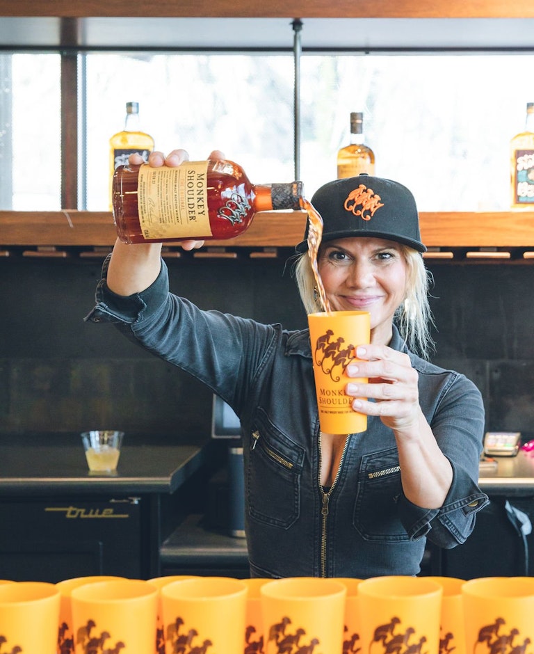woman pouring Monkey Shoulder whiskey into a cup