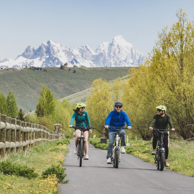 Three people biking on a bike trail on E-Bikes with the Teton mountain range in the background