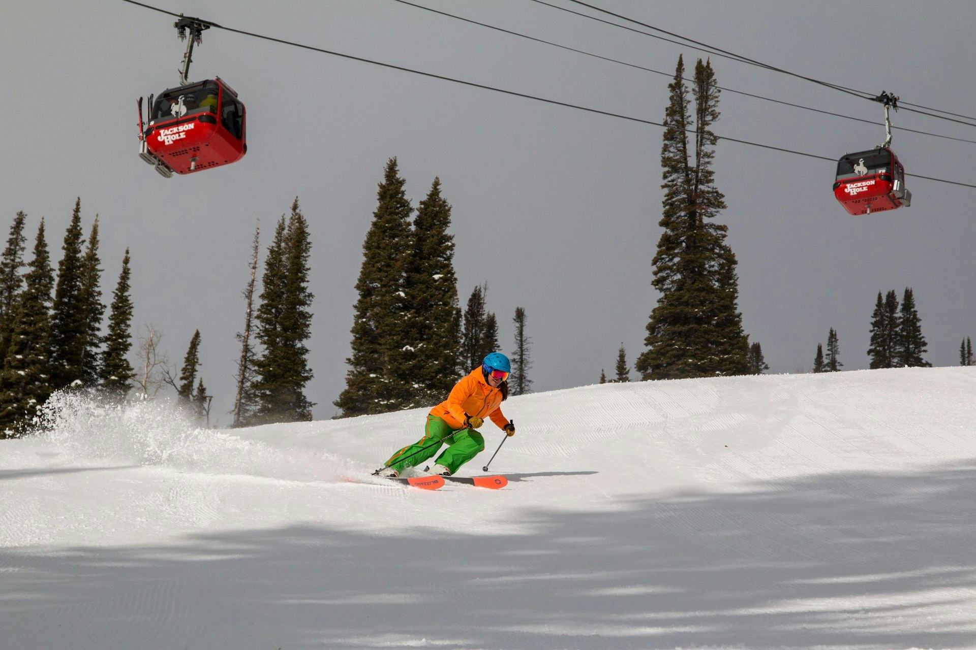 Person skiing a groomed run with gondola in background