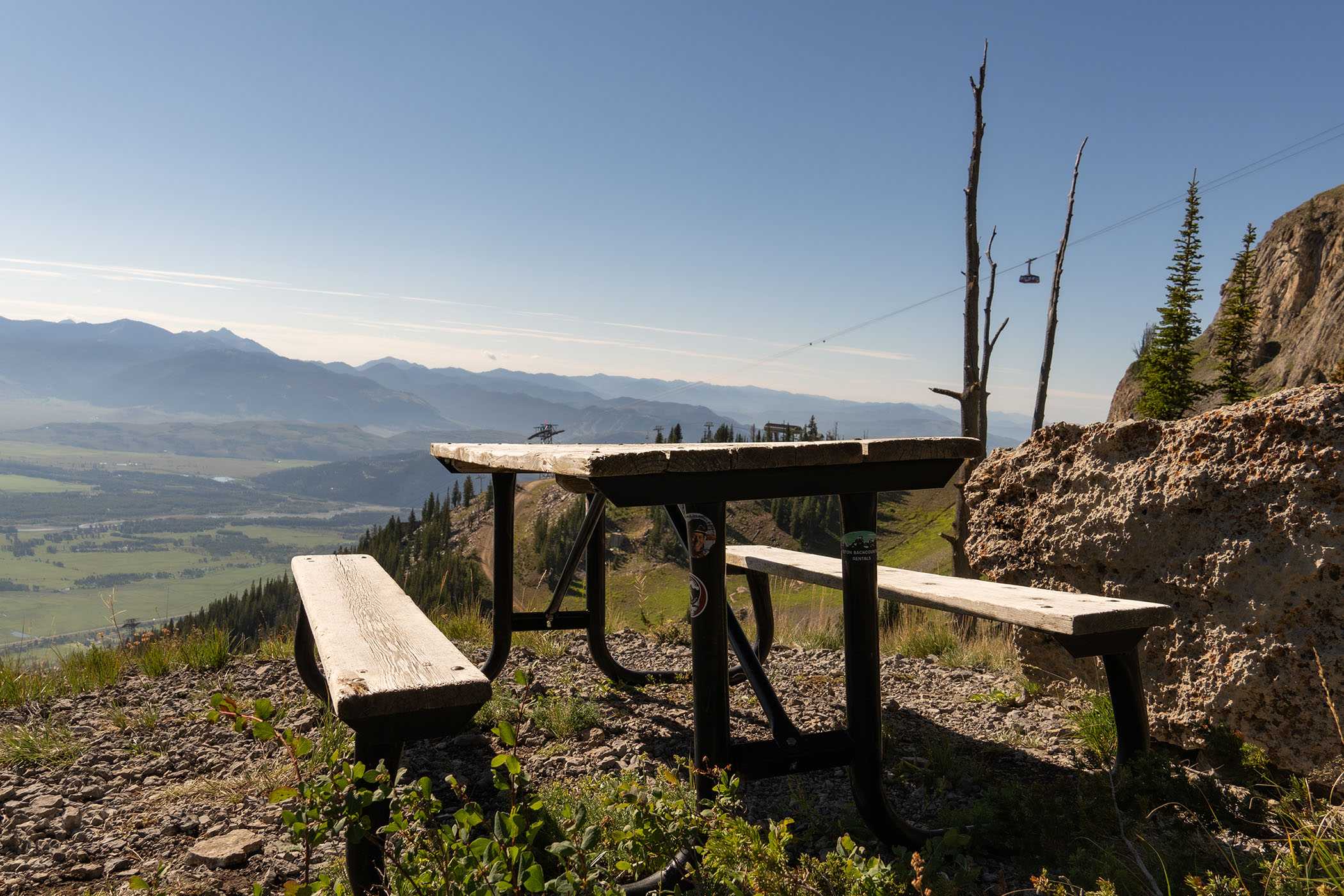 A picnic bench along the Cirque trail with the Tram flying in the air in the background