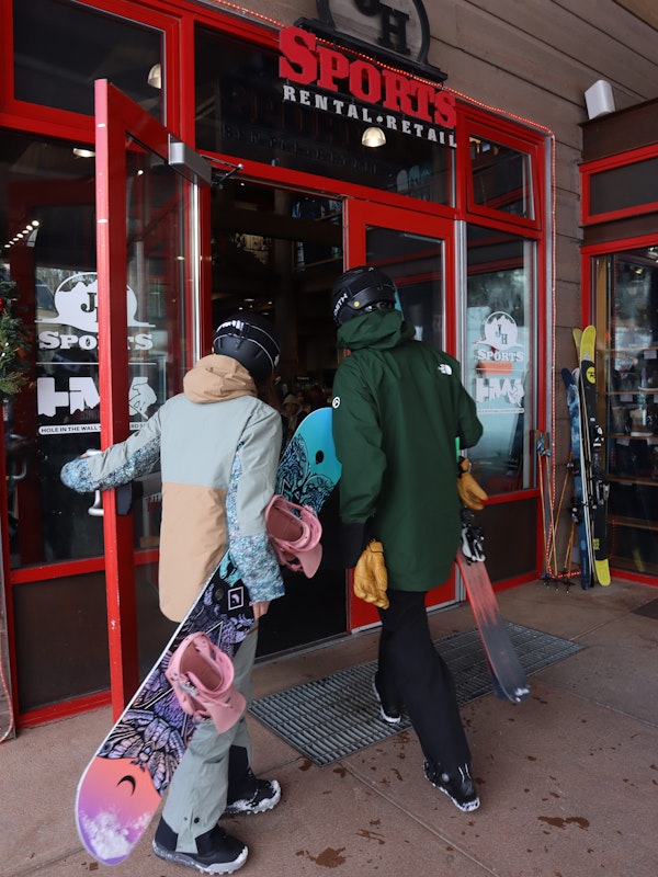 A skier and snowboarder walking into JH Sports