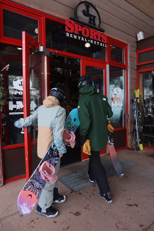 A skier and snowboarder walking into JH Sports