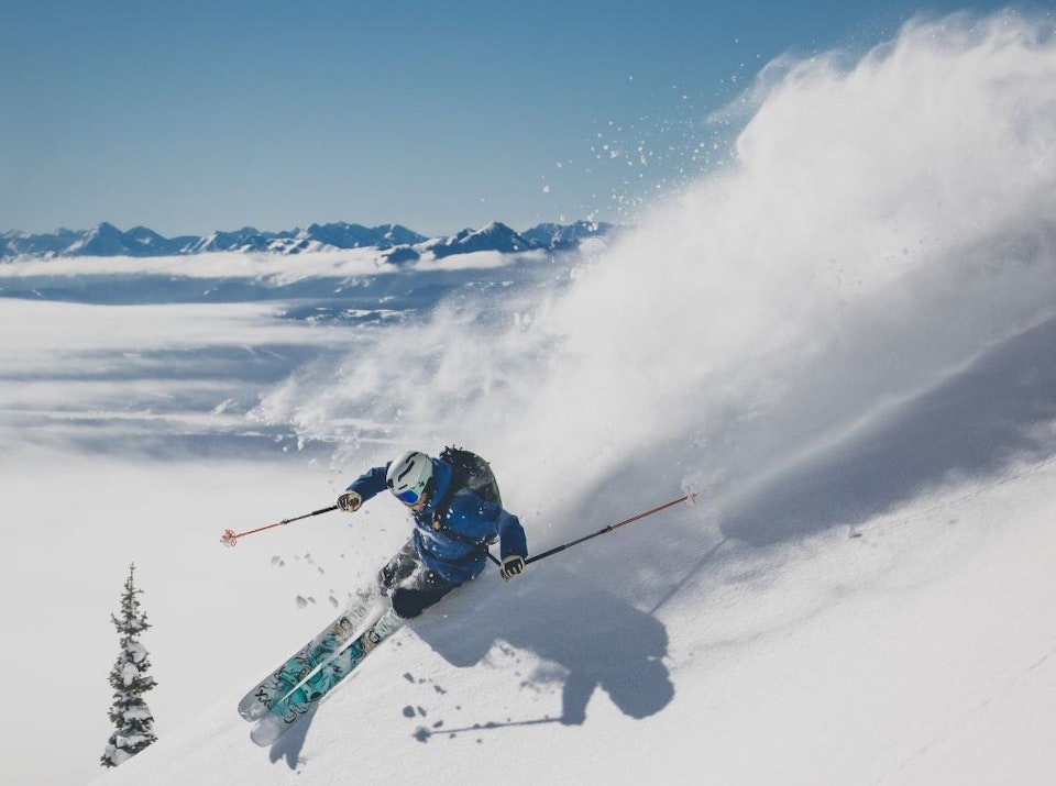 Skier making a big turn in deep powder with the Jackson Hole valley in the background on an inverted day.