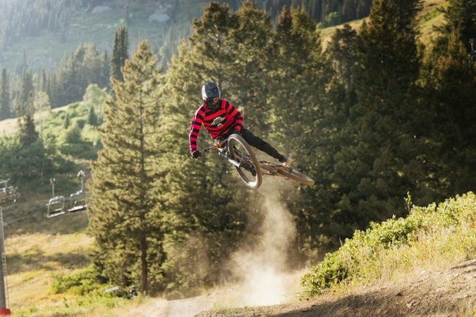 mountainer biker doing whip jackson hole bike park, lush trees in background