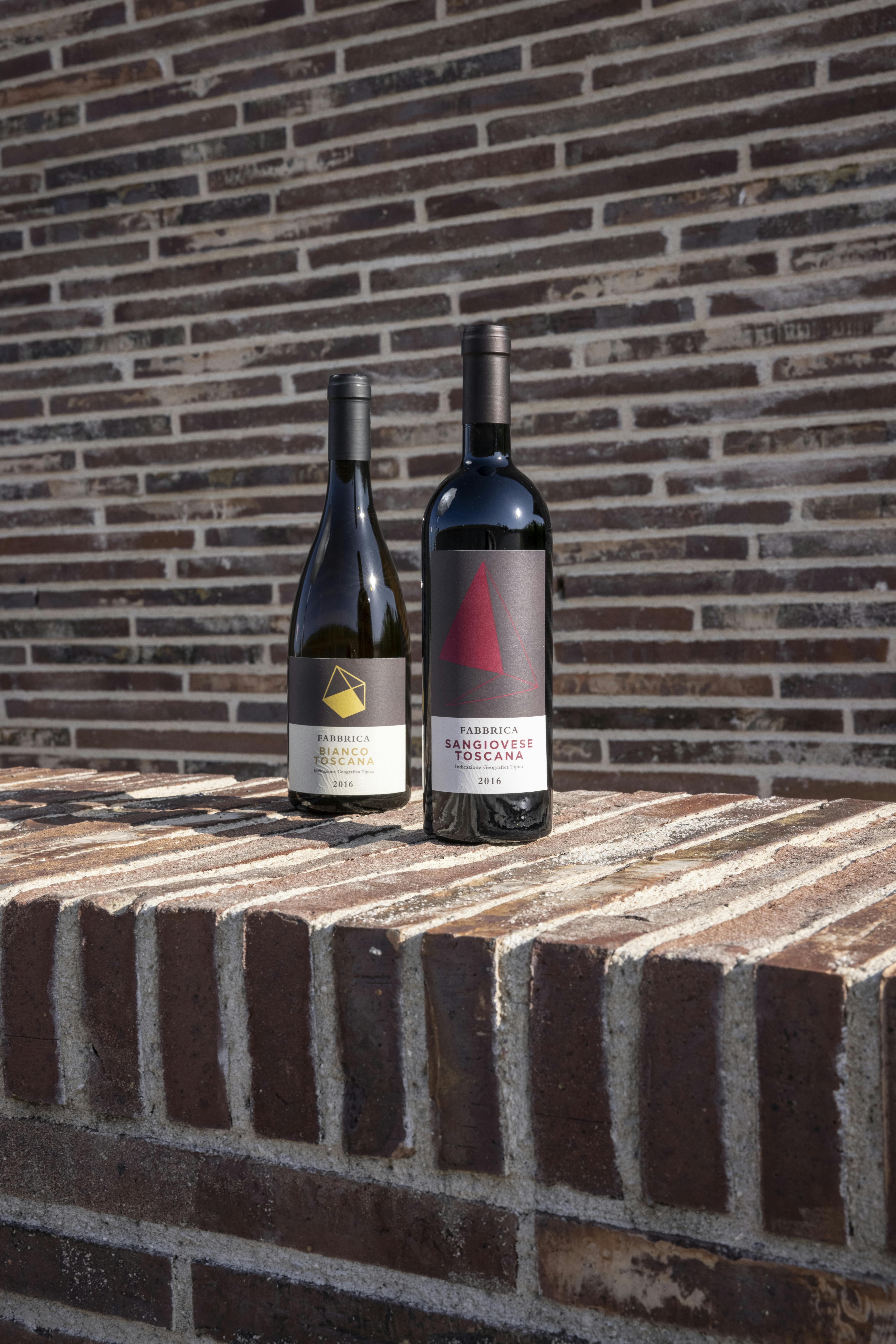Una bottiglia di vino bianco e una bottiglia di vino rosso Sangiovese con un muro di mattoni della cantina sullo sfondo