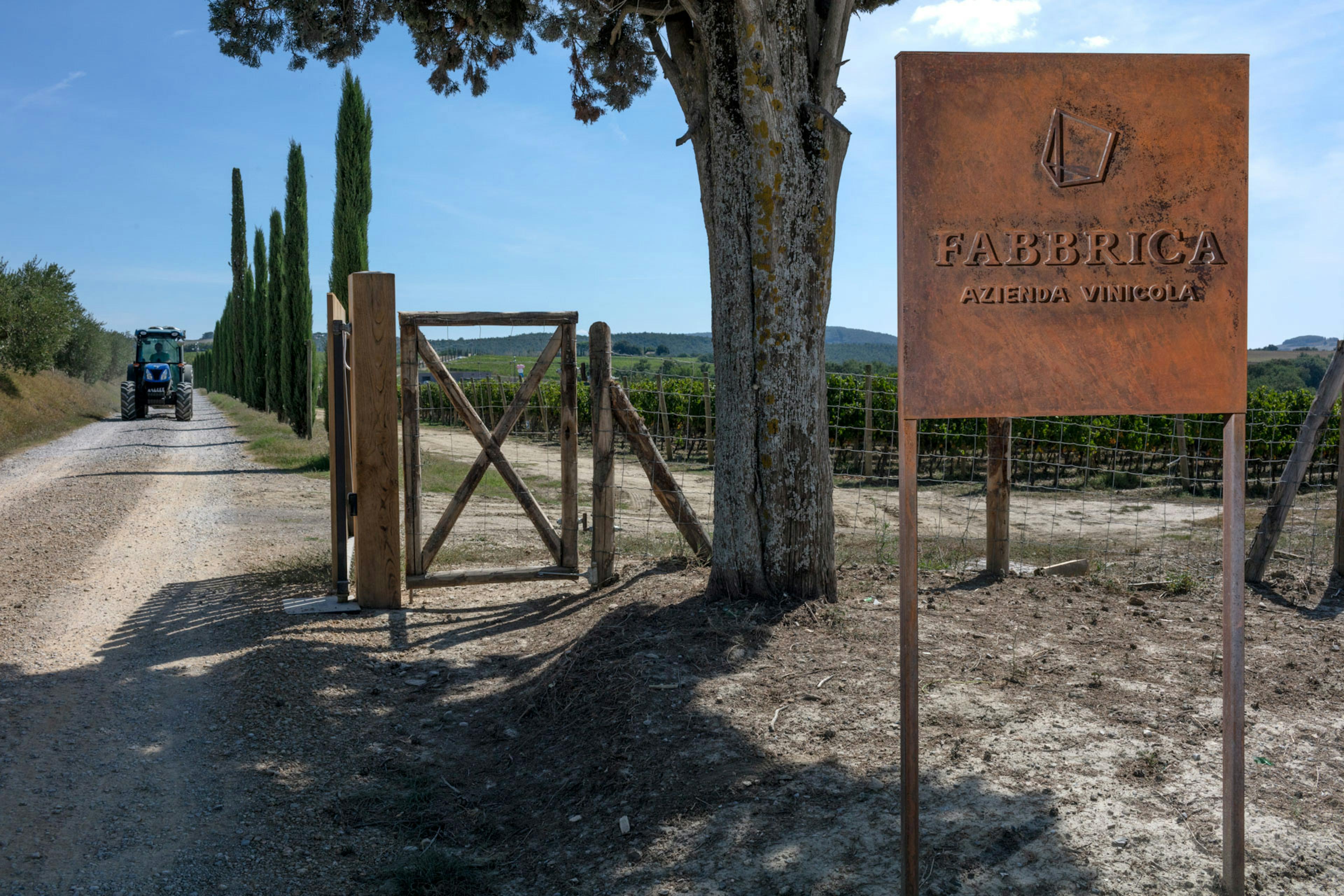 Entrance of Fabbrica with a tractor on the strada bianca, cypresses alongside and the sign of the winery