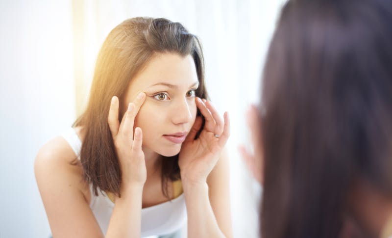woman examining her eyes in the mirror