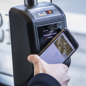 Image d'une personne tenant son téléphone portable au-dessus d'une machine de paiement dans un bus pour payer un ticket.