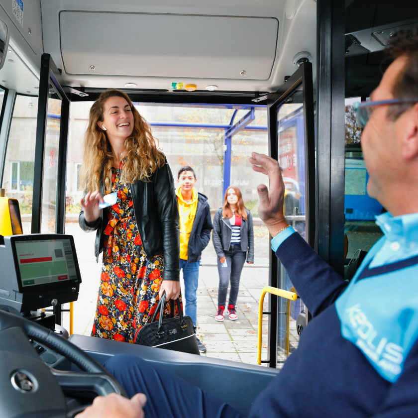 A young woman gets on a bus smiling at the driver, ready to validate.