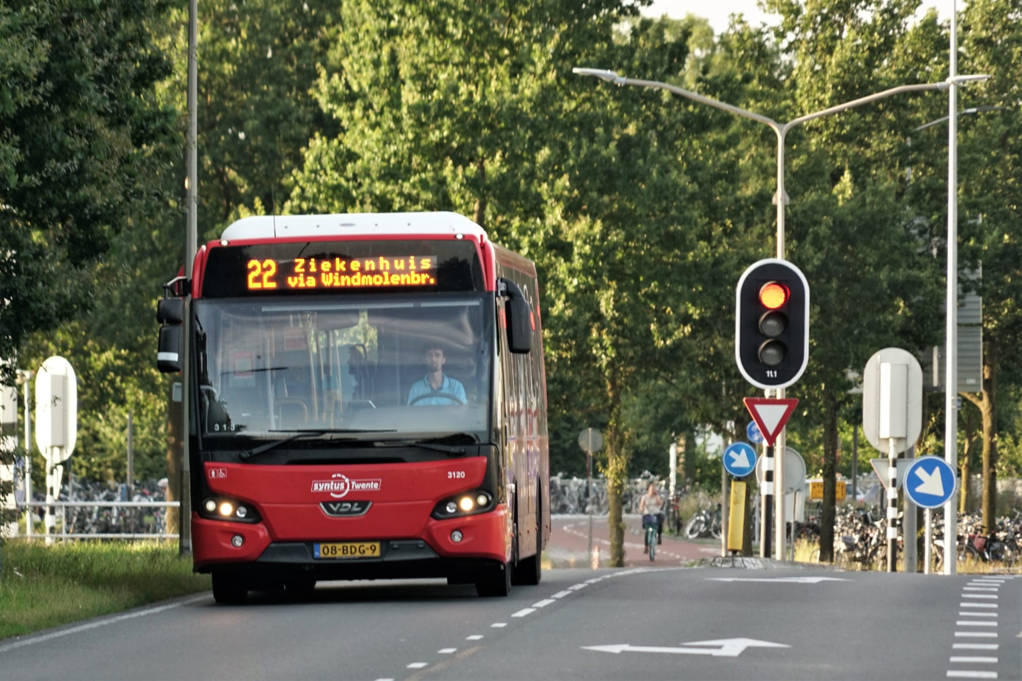 A red bus from the region of Twente is driving on a road.