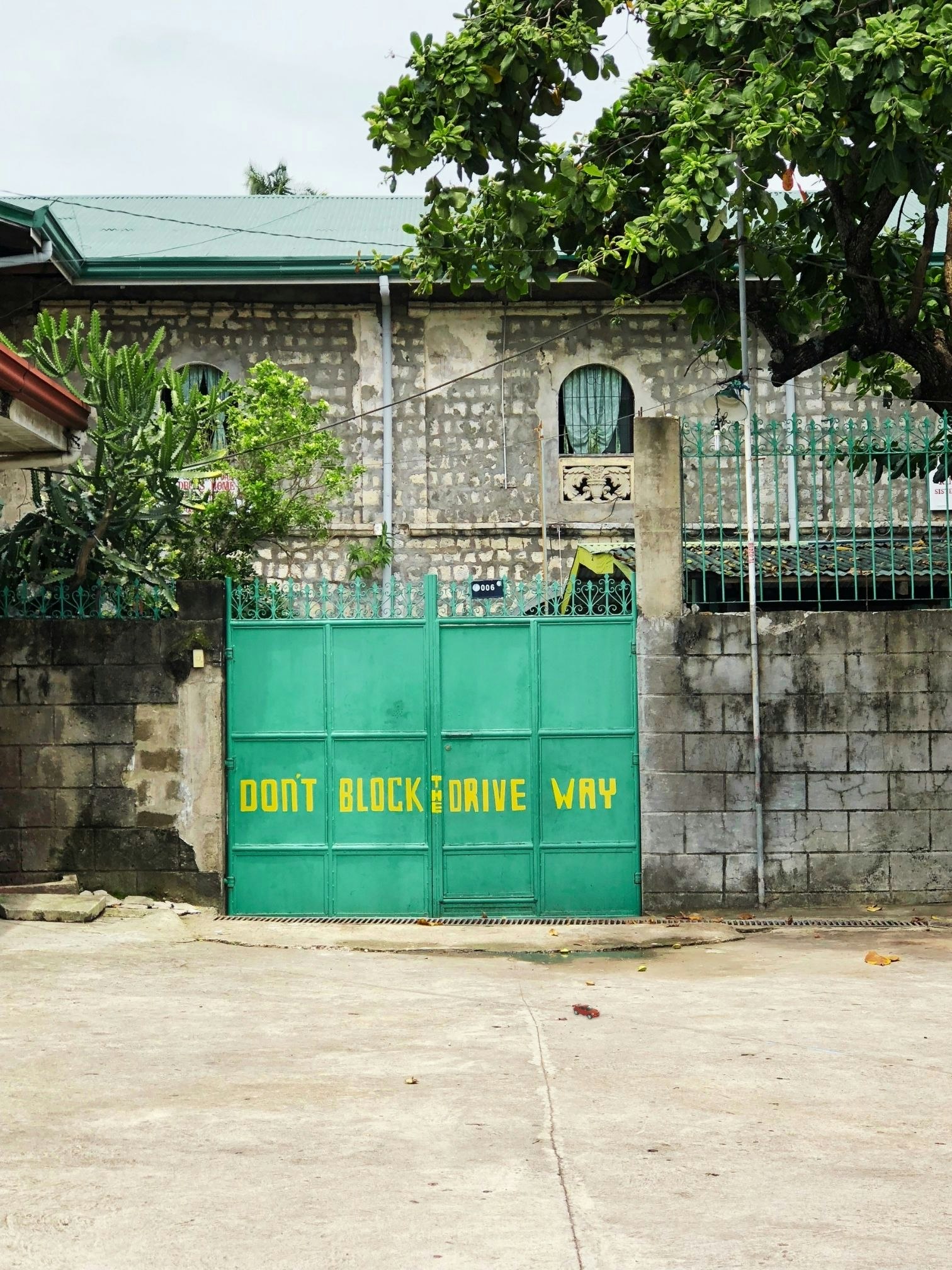 A toy car blocks a gate emblazoned with a hand-painted sign 'Don't block the drive way'; located in the author's childhood district, Cubao, Philippines, 2018 | Photo: Mariam Arcilla