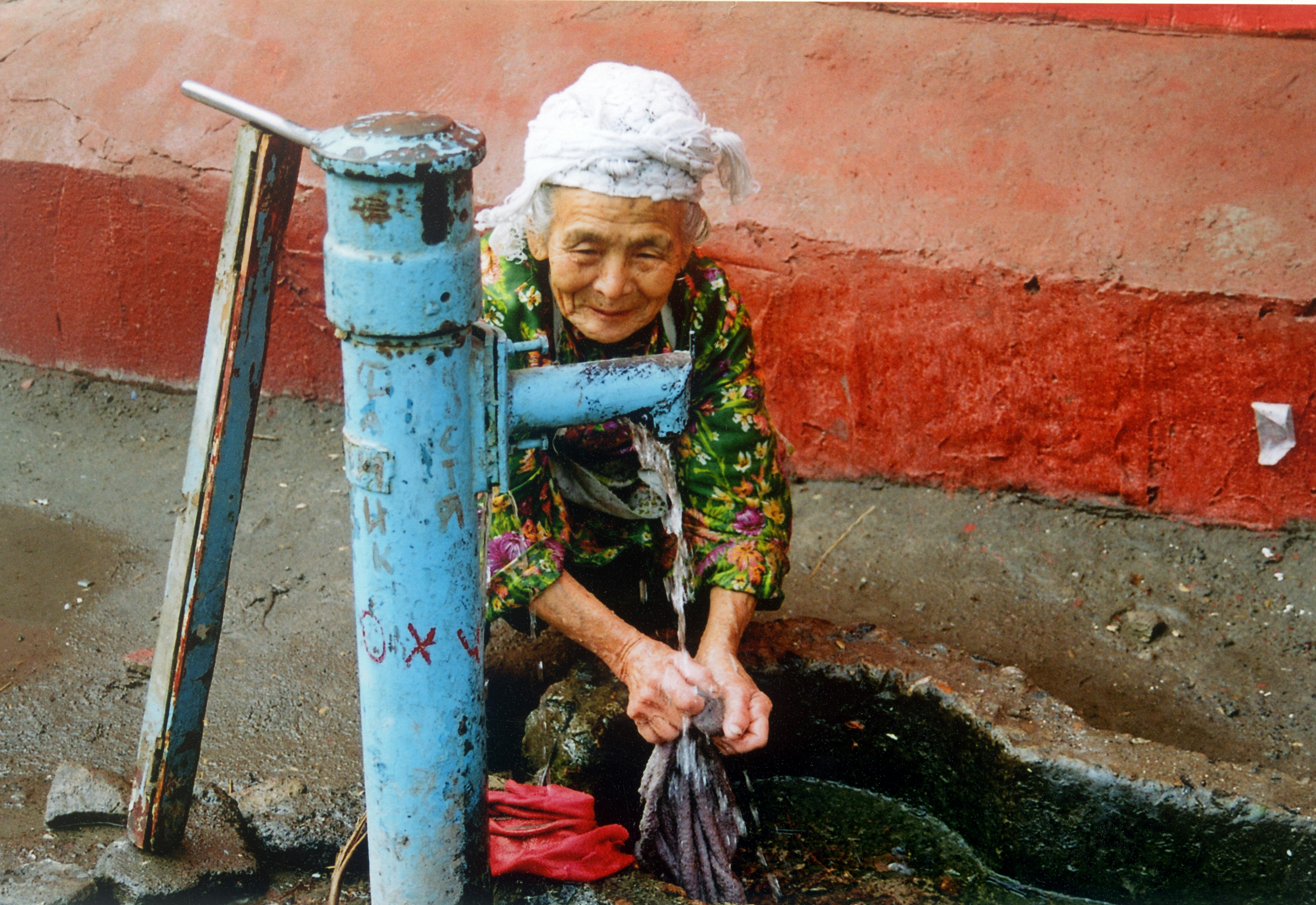 An elderly woman washing her hands under a blue tap.