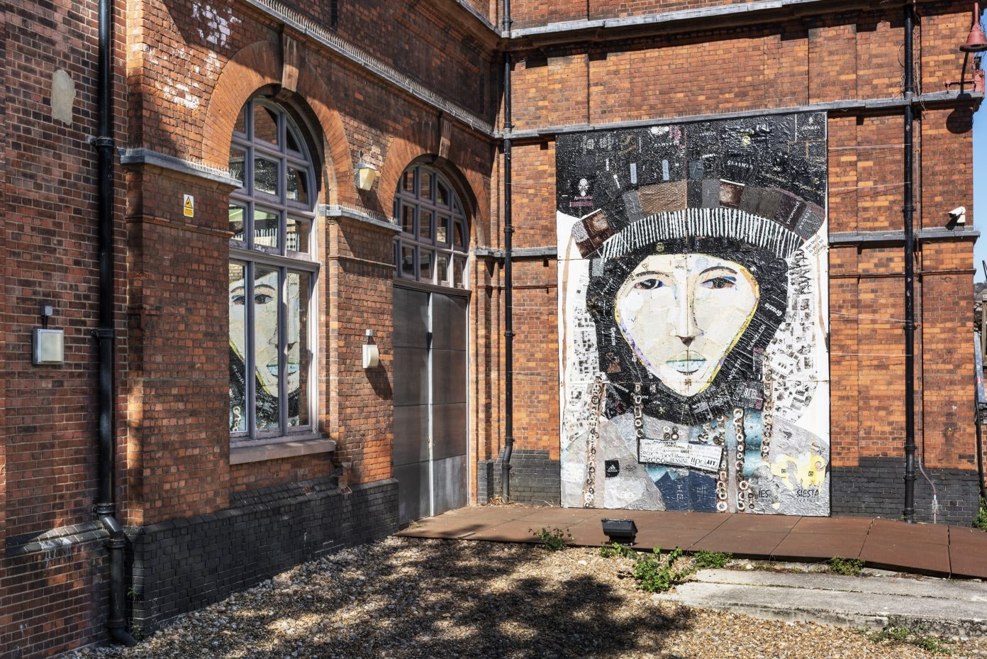 Two red brick walls, one with a large artwork depicting a face.