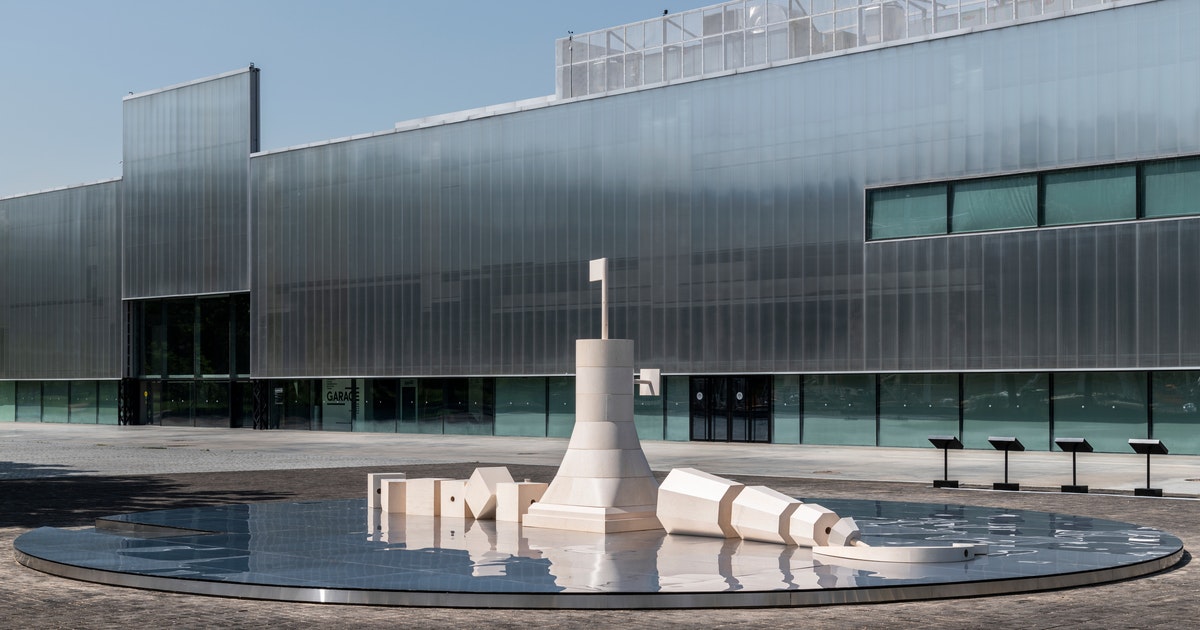 A large sculpture outside a building.  The sculpture is white and depicts a tower with a flag in the centre.