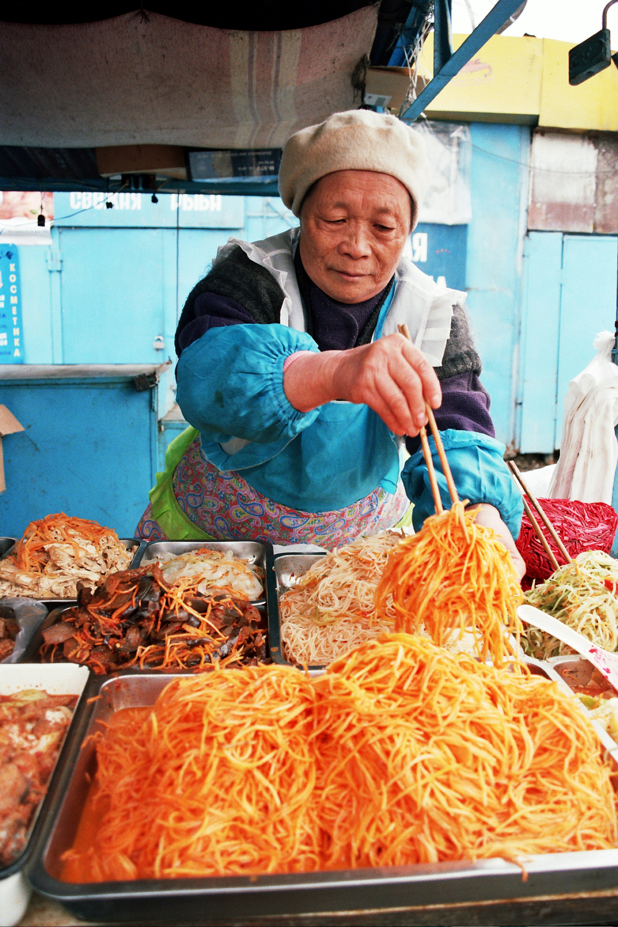 An elderly woman serving food with chopsticks