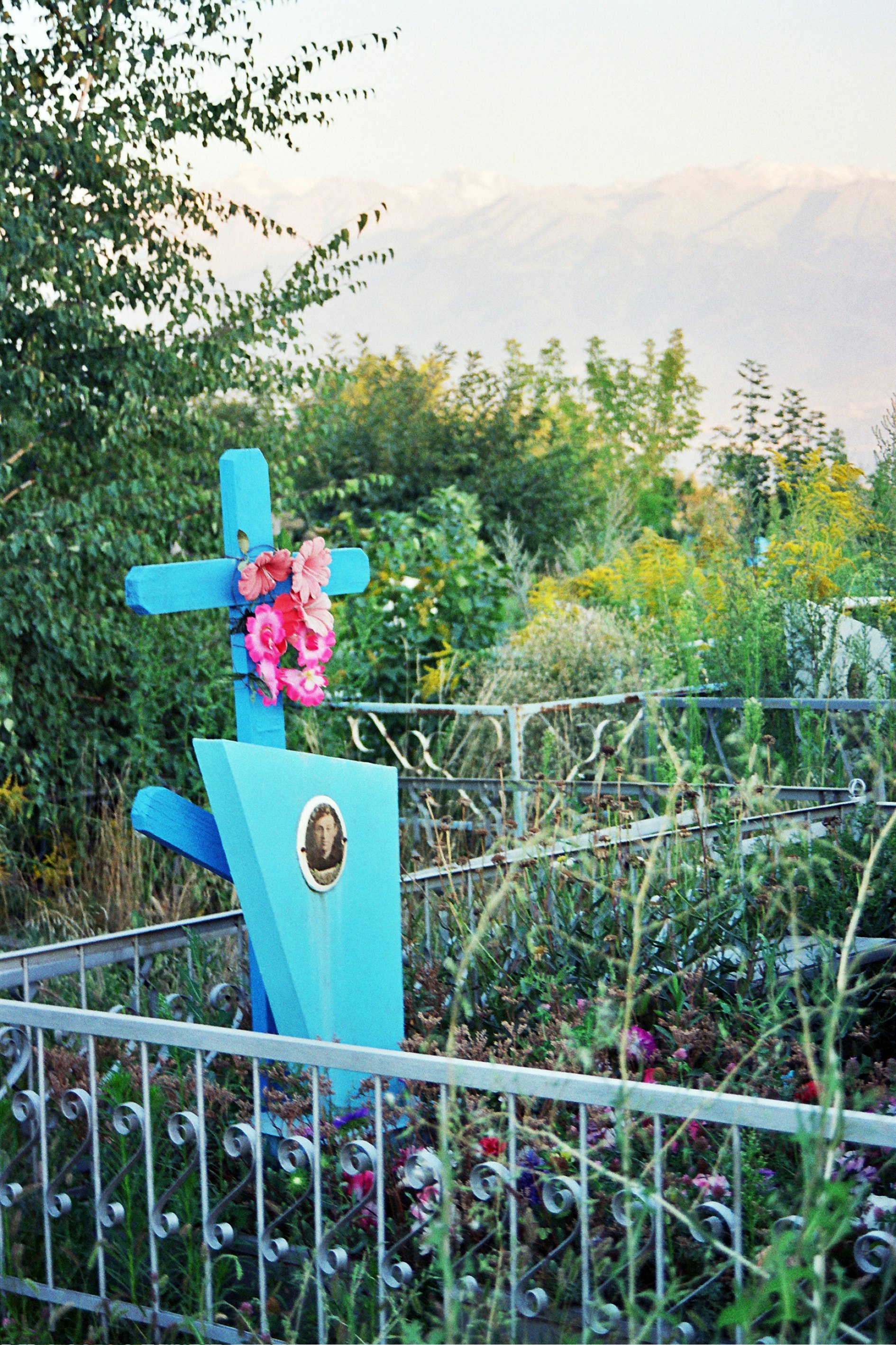 Blue cross with flowers in a garden behind a fence.