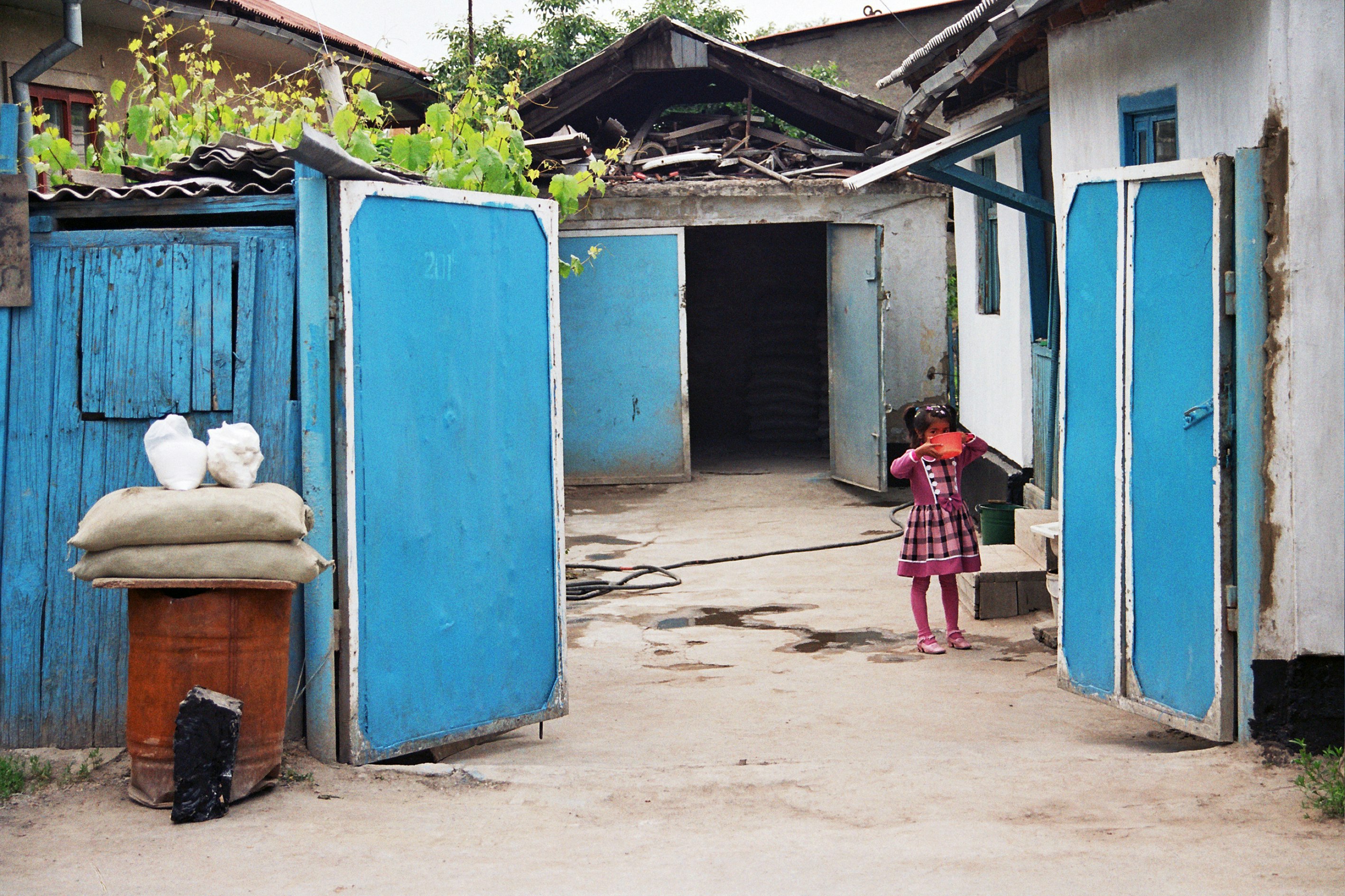 A small child drinking from a red bowl. They are standing in between a blue gate.