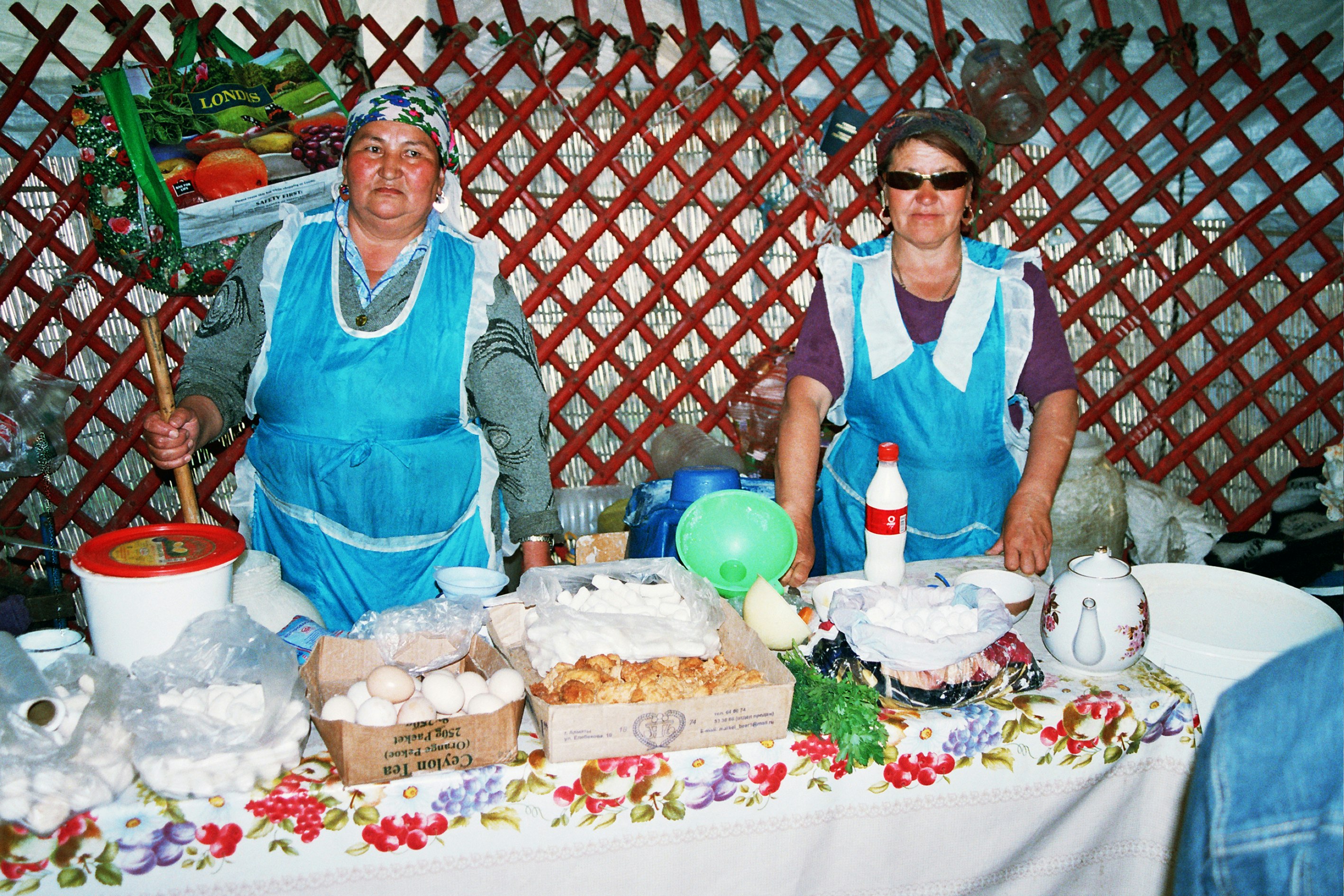 Two adults behind a table of food wearing blue and white aprons.