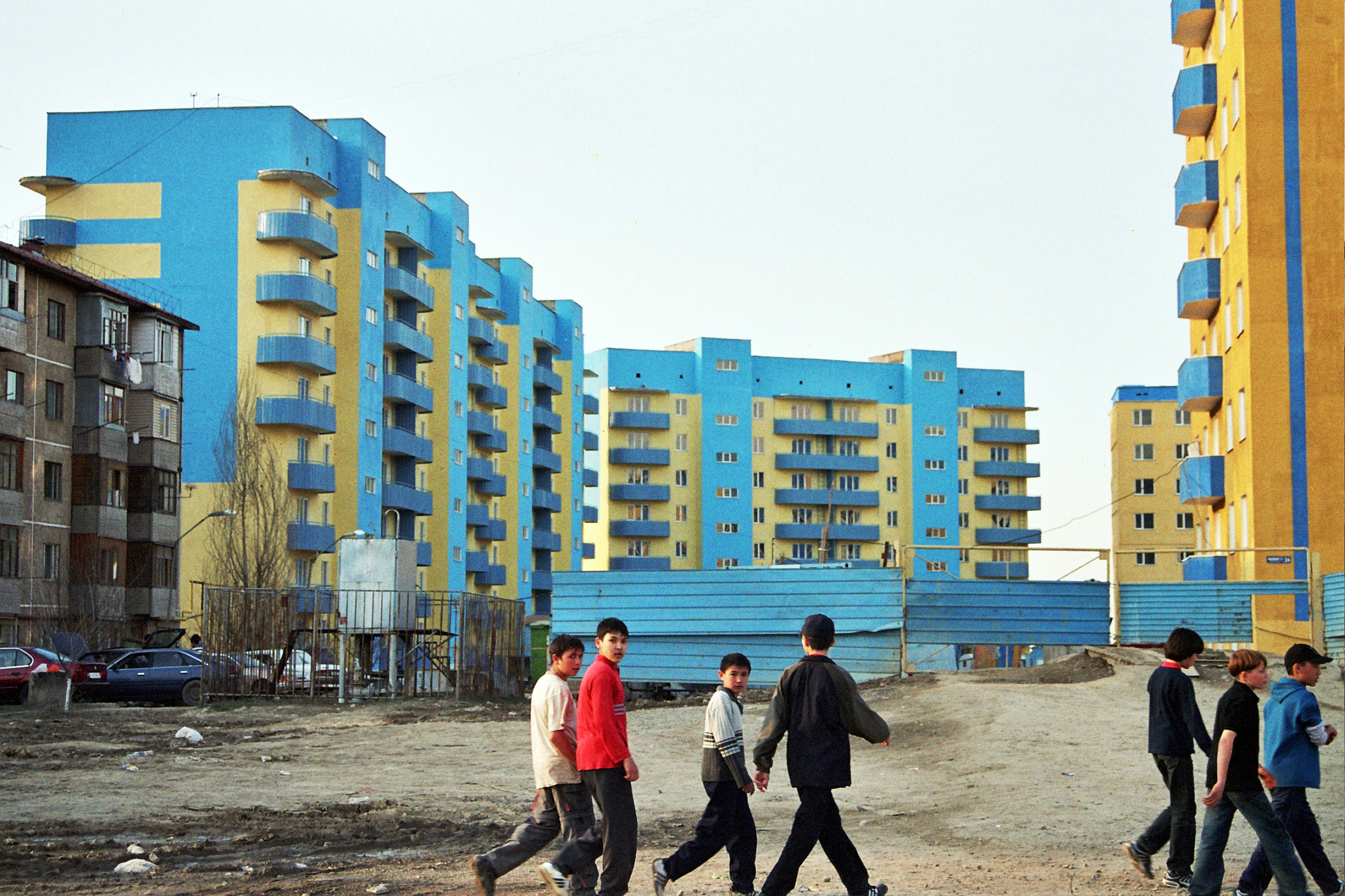 A group of teenagers walk in front of a uniform group of yellow and blue buildings.