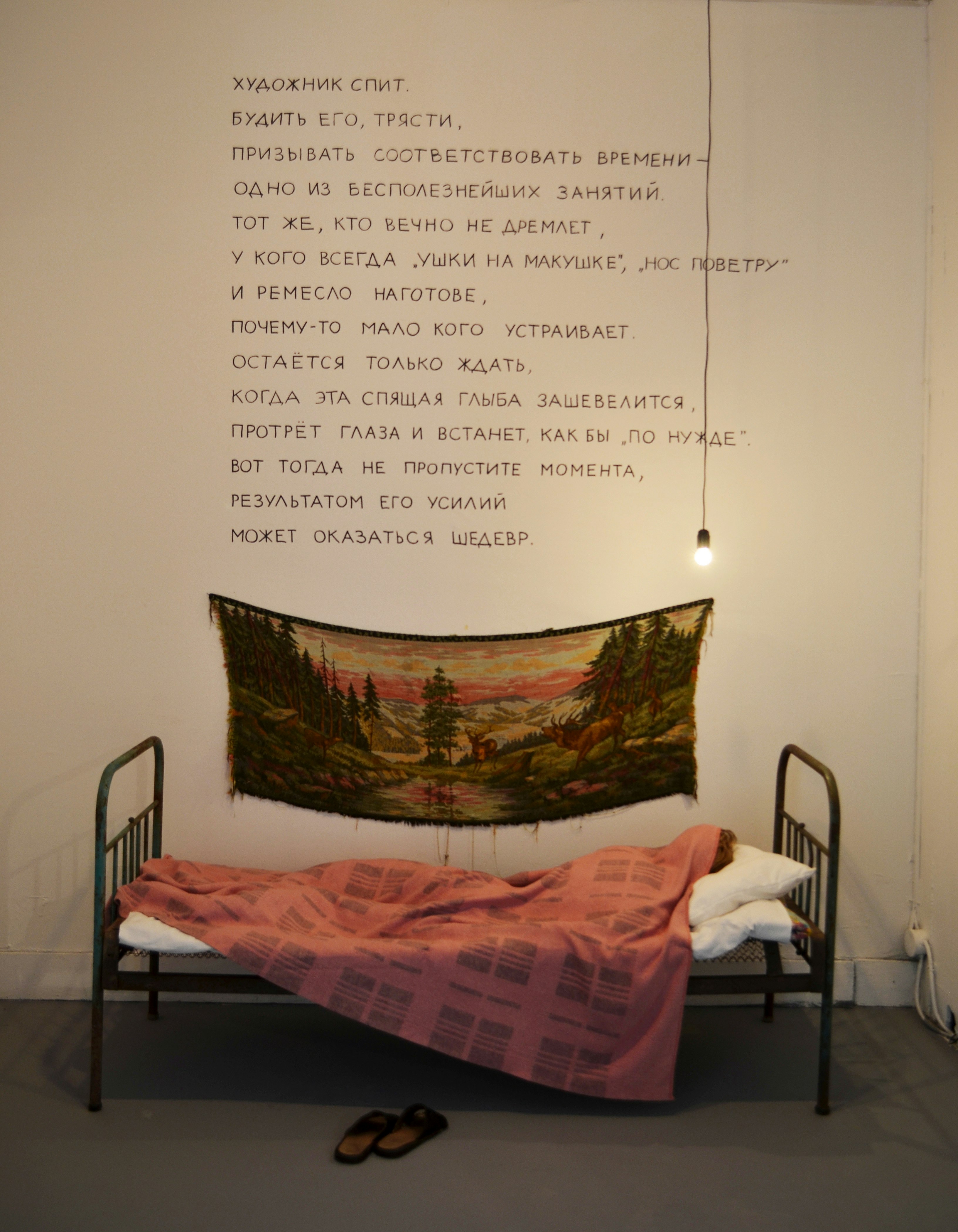 A bed underneath text. English translation reads 'The Artist is Asleep. / To wake him, to shake him, to urge to conform to his time is an utterly useless endeavour. / But the one who is always wide awake, always is “all ears”, knows “which way the wind blows” / and has his craft at the ready, does not suit many for some reason. / All one can do is to wait for the sleeping boulder to stir, rub open his eyes and get up / You only have to wait for the sleeping block to wake up, rub open his eyes and get up as if to relieve himself. / Well then don’t let the moment slip. His efforts may result in a masterpiece. *Text courtesy of the artists and Aspan Gallery.