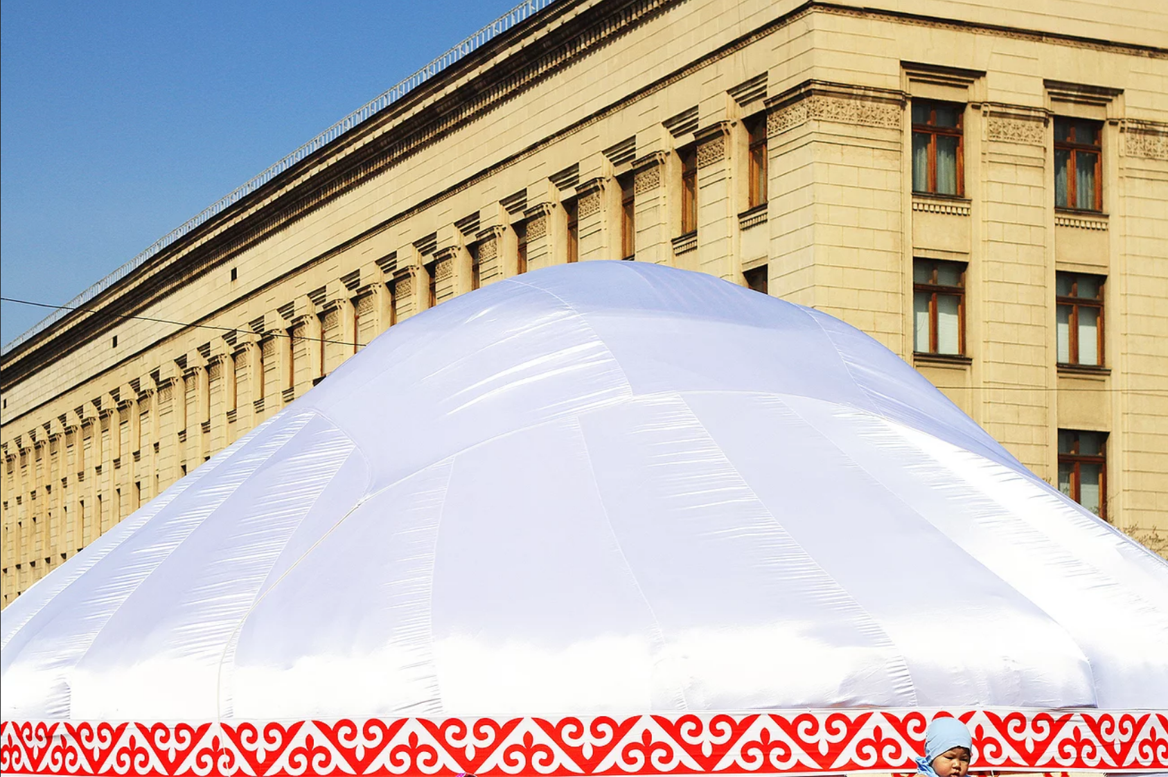 A large white dome in front of a yellow building. A child's face sits in front of the dome.