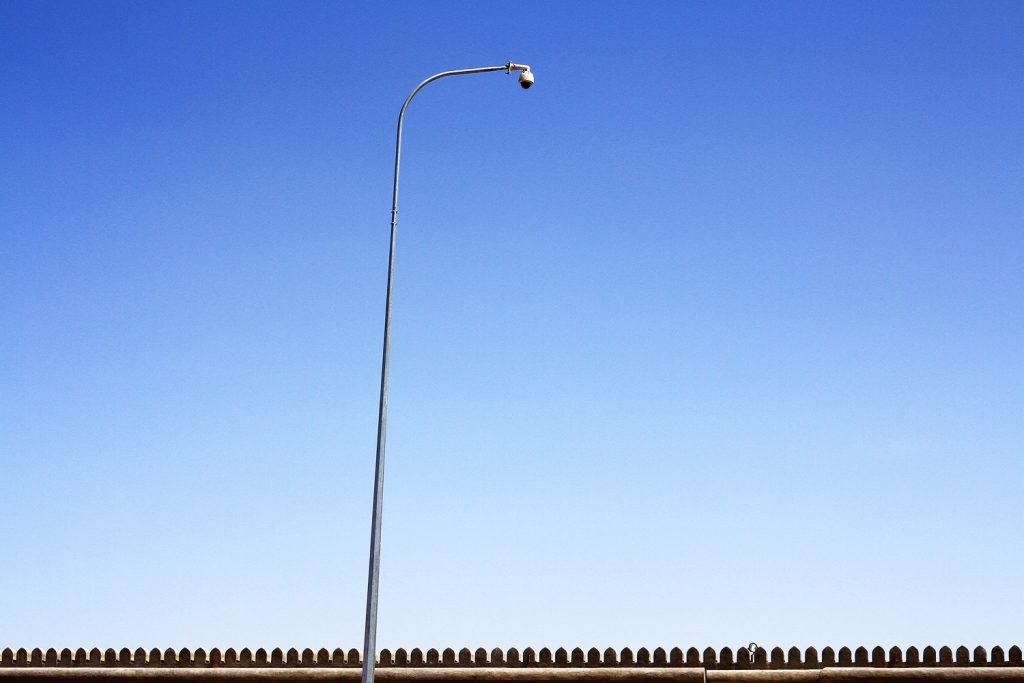 A streelight pole and a fence sit in front of a bright blue sky