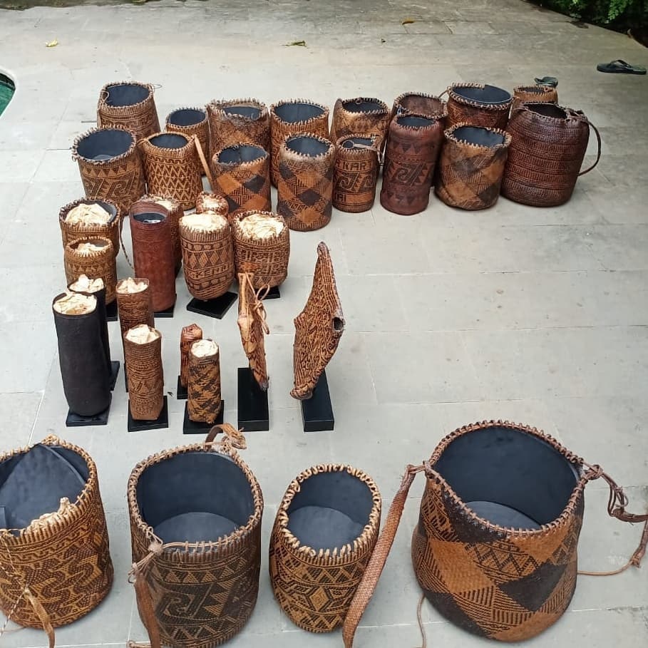 A selection of woven baskets and textiles named 'betenun' arranged on concrete ground