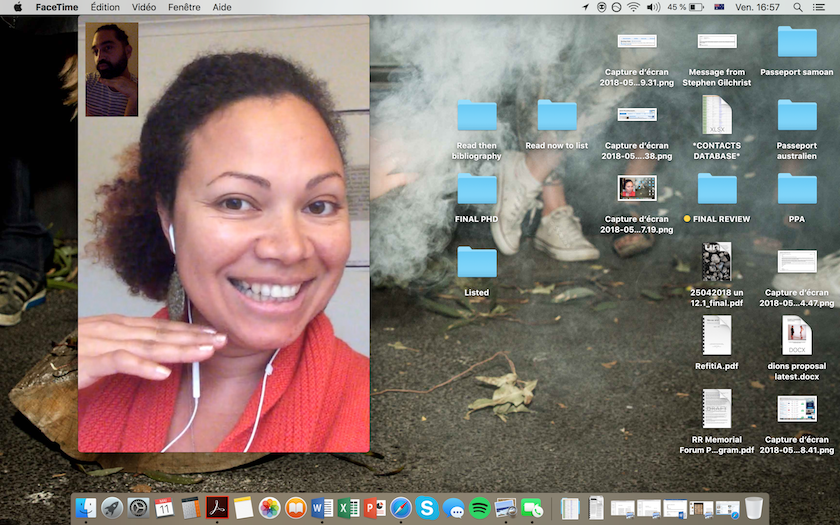 A Pasifika woman with brown curly hair tied back in a pony tail smiles on a video call.