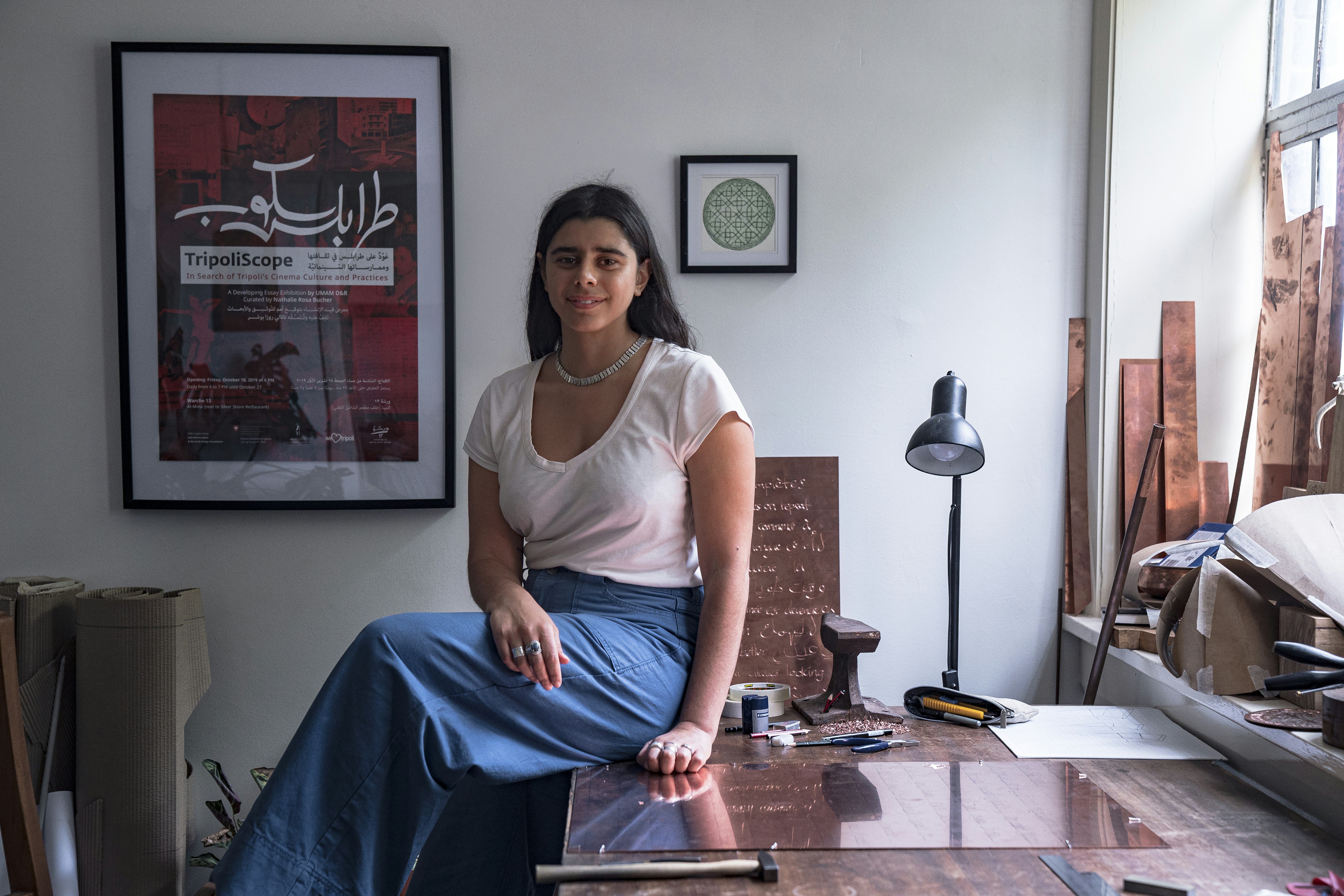 A photo of artist Shireen Taweel sitting on a workbench in her studio.