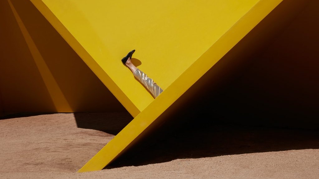 A production still from Eugenia Lim's The Australian Ugliness, depicting her raised leg as she sits between yellow slabs.