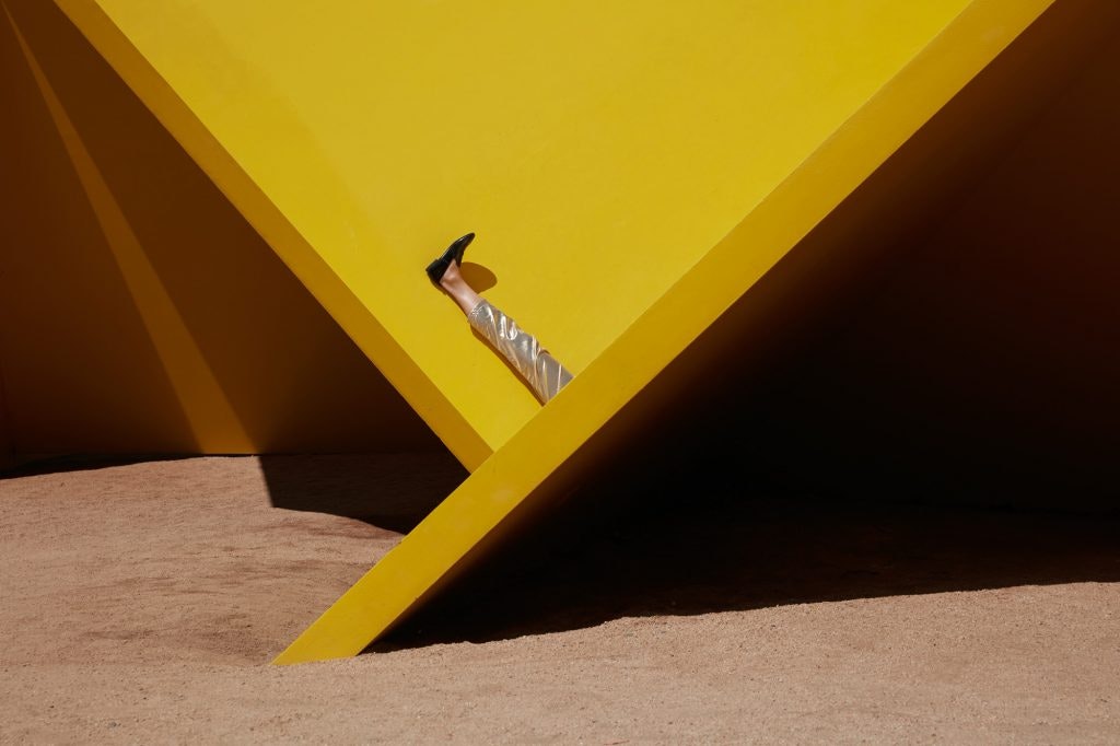 A production still from Eugenia Lim's The Australian Ugliness, depicting her raised leg as she sits between yellow slabs.