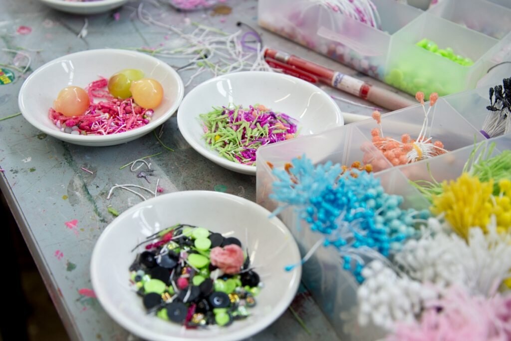 A table with bowls and containers full of decorations from which to make zodiac flower charms.