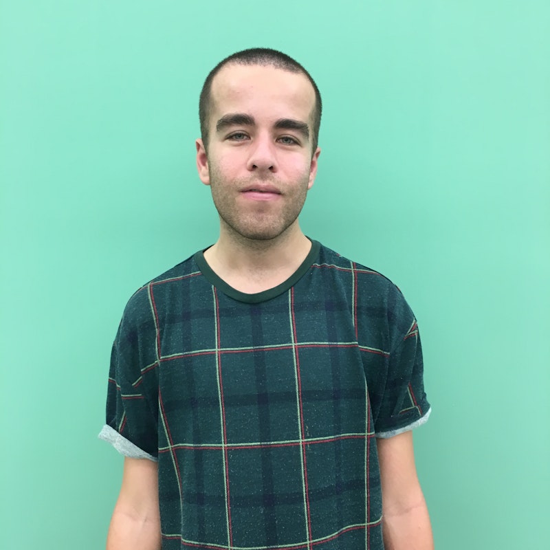 Rob stands in front of a green wall with a smile on his face and wears a green checkered t-shirt