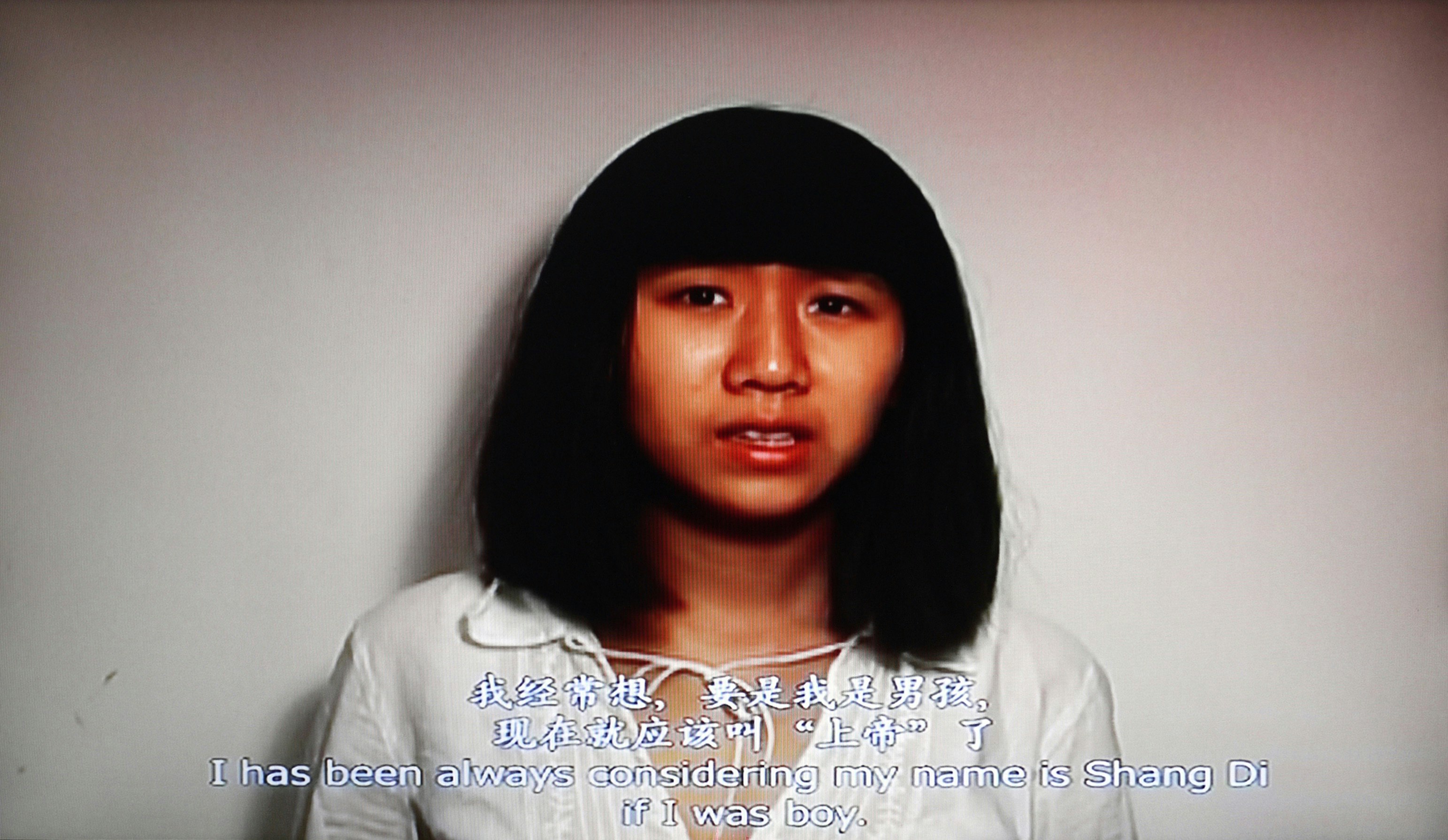 A woman stands in the centre of the frame looking at the camera. Text translation reads 'I has ben always considerring my name  is Shang Di if I was a boy'