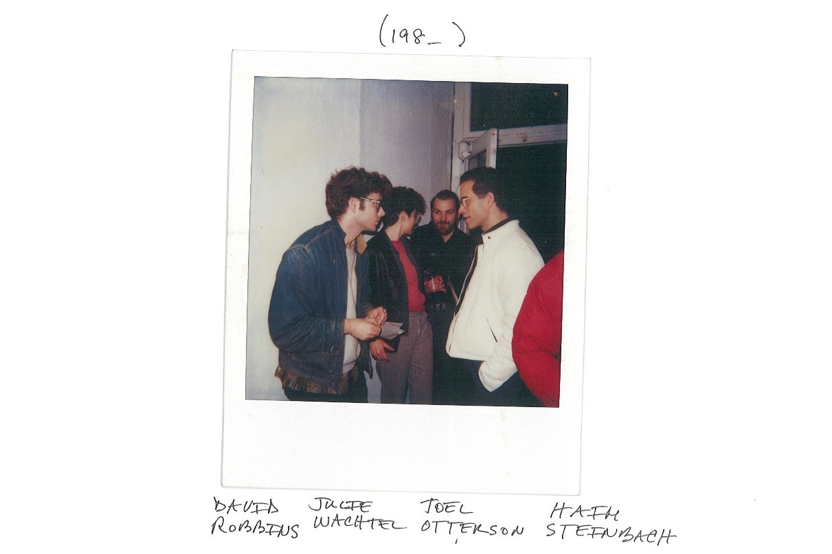 A Polaroid of four short-haired artists speaking in a room. Handwritten underneath are the names David Robbins, Julie Wachtel, Joel Otterson and Haim Steinbach.