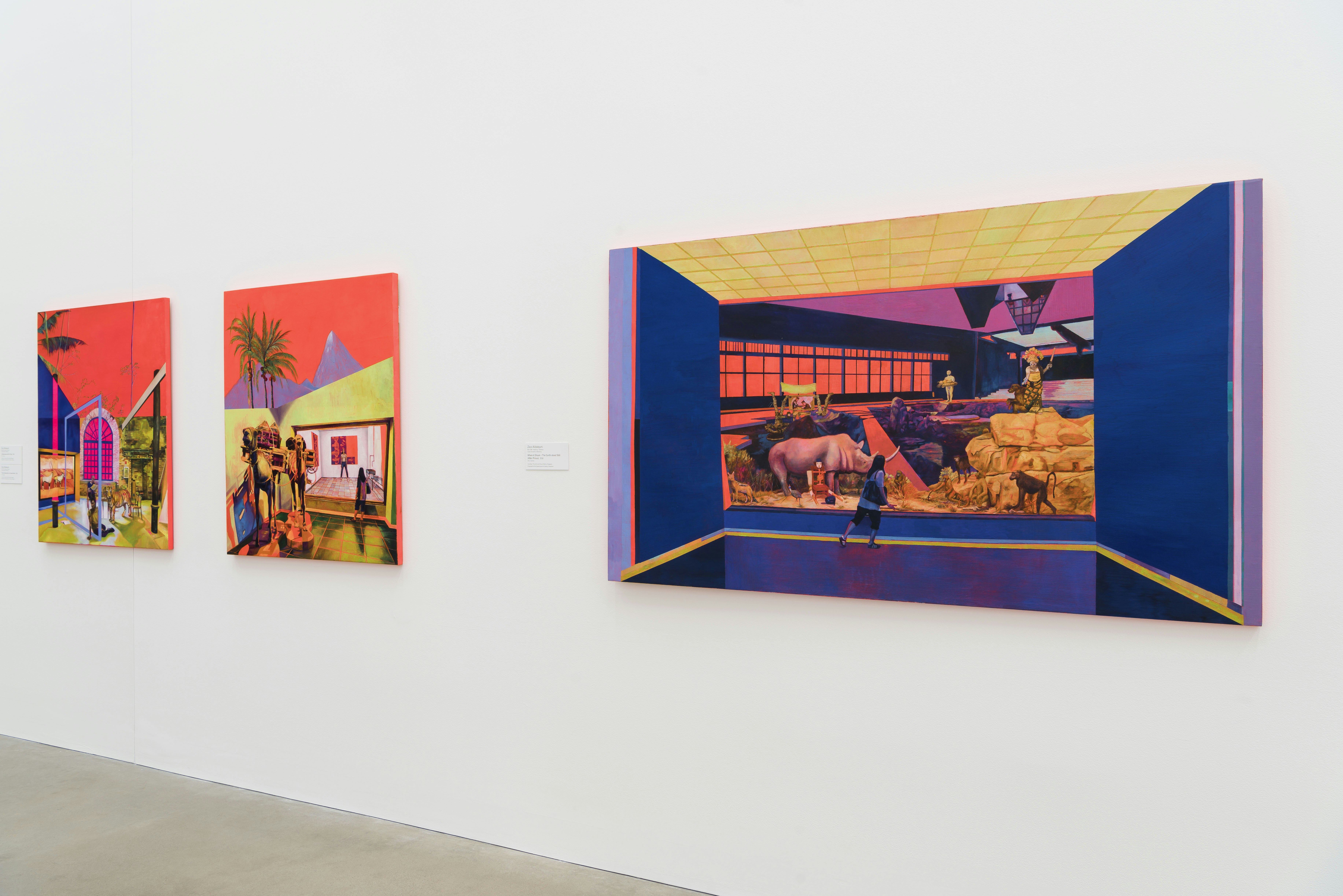 Three paintings hanging on a gallery wall at QAGOMA: the two left paintings show a tropical architectural space under a bright orange sky, while the right painting shows a figure looking at animals in a reflective blue-walled space.